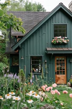 a green house with lots of flowers in the front yard and windows on each side