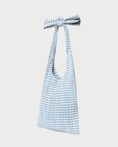 Pleated tote bag in blue gingham fabric. Features a shoulder strap with playful bow detail, an exterior cotton logo, and an open interior. Cotton Tote Shoulder Bag For Picnic, Spring Picnic Cotton Bag, Picnic Tote Shoulder Bag With Adjustable Strap, Tote Shoulder Bag With Adjustable Strap For Picnic, Blue Rectangular Picnic Bags, Casual Gingham Shoulder Bag For Picnic, Gingham Cotton Bags For Summer, Blue Tote Bag For Picnic, Summer Gingham Cotton Bags