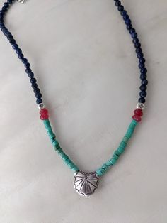 This 17-inch necklace strings lovely blue Lapis and Turquoise stone beds with Hill tribe silver and dark pink accents.  The shell-like silver bead in the center is 1/2 inch. Blue Turquoise Sterling Silver Necklace In Bohemian Style, Blue Beaded Turquoise Amulet Necklace, Blue Beaded Amulet Style Turquoise Necklace, Bohemian Blue Turquoise Sterling Silver Necklace, Spiritual Turquoise Sterling Silver Beaded Necklaces, Turquoise Sterling Silver Spiritual Beaded Necklace, Spiritual Turquoise Beaded Necklace In Sterling Silver, Beaded Turquoise Necklace In Sterling Silver, Blue Turquoise Necklace With Round Beads In Sterling Silver