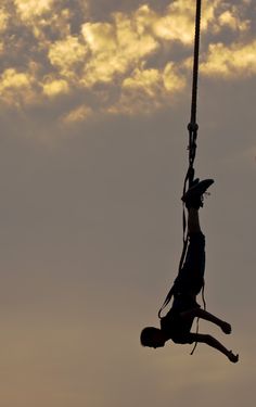 a man hanging from a rope in the sky with his feet dangling off an object