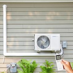 a person is checking the air conditioner in front of a house with green plants