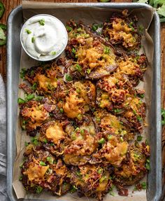 a tray filled with fried potatoes and green onions next to a bowl of ranch dressing