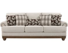 a white couch with brown and tan pillows on it's back cushions are in the shape of leaves