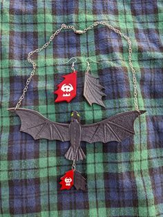 two necklaces with bats on them are sitting on a green and blue checkered shirt