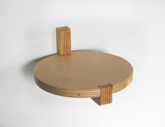 a round wooden shelf with two brackets on the top and one at the bottom, against a white wall