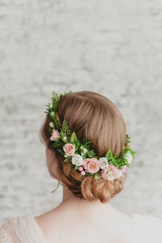 a woman with flowers in her hair wearing a flower crown on her head, against a white brick wall