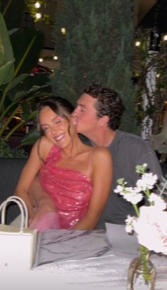 a man and woman sitting next to each other at a table with flowers in front of them