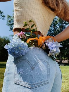 a woman is holding her back with flowers in it's pocket and jeans on the side