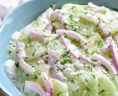 a blue bowl filled with cucumber and onions on top of a wooden table