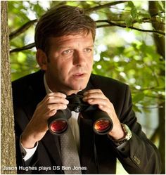 a man in a suit looking through binoculars at the camera while standing next to a tree