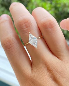 a woman's hand with a diamond ring on top of her finger and trees in the background