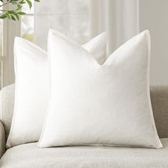 two white pillows sitting on top of a couch next to a potted green plant