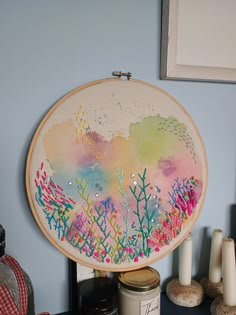 an embroidery project is displayed on a table next to candles and other items in front of a blue wall