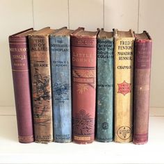 a row of old books sitting on top of a white shelf next to each other