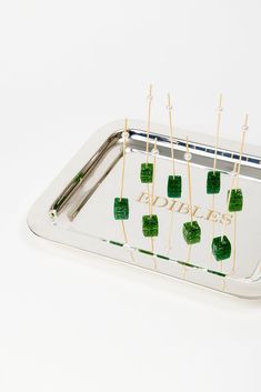 a metal tray with green squares and toothpicks on it, sitting on a white surface