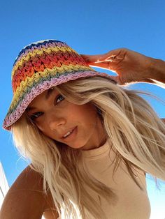 a woman with blonde hair wearing a multicolored crochet hat and posing for the camera