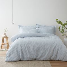 a bed with blue sheets and pillows in a room next to a potted plant