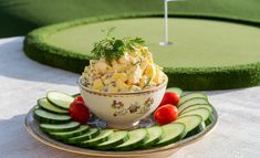 a bowl filled with food sitting on top of a plate next to cucumbers