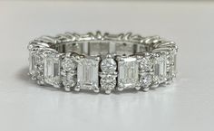 an emerald cut diamond ring on a white surface with diamonds surrounding the band and side stones