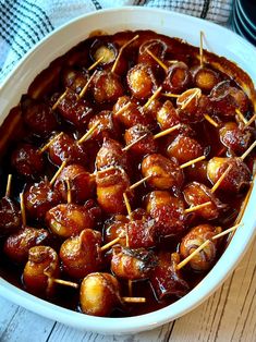 a white dish filled with meat covered in sauce and toothpicks on top of skewers