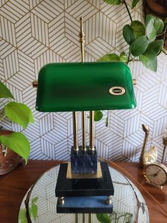 a green lamp sitting on top of a glass table next to a clock and potted plant