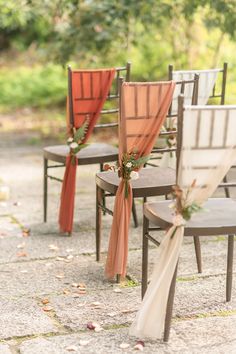 chairs with orange sashes are lined up on the ground for an outdoor wedding ceremony