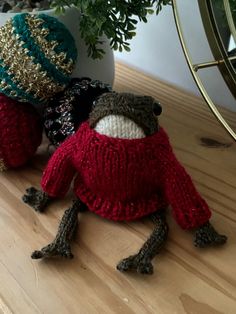 two knitted frog dolls sitting next to each other on a wooden table with a potted plant in the background