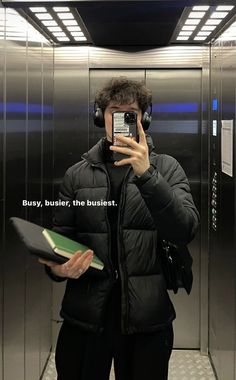 a man taking a selfie in an elevator with headphones and holding a book