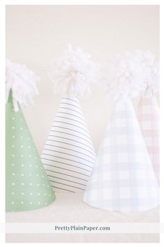 three paper party hats with pom poms on the top, one in white and one in green