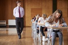 students sitting at desks in an empty classroom with one male teacher walking behind them