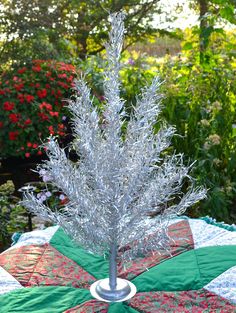 a silver christmas tree on top of a quilt covered table cloth in a garden area