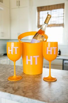 two wine glasses and a bottle in a bucket on a kitchen counter with white cabinets