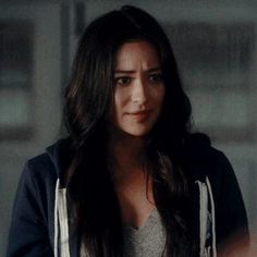 a woman with long dark hair wearing a hoodie and looking at someone in the mirror