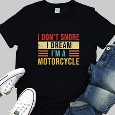 "Rev up your wardrobe with our funny \"I Don't Snore, I Dream I'm a Motorcycle\" biker shirt. This high-quality, comfortable tee is a top gear choice for any motorcycle rider, sure to add horsepower to your style. Decked in colorful, vibrant text, this men's shirt isn't just a piece of clothing, it's a conversation starter. Whether you're thundering down the highway or kicking back at a local café, it's designed to get laughs and admiring nods from fellow bikers and friends alike. Seeking the pe Cotton Biker T-shirt With Letter Print, Cotton Biker Tops With Letter Print, Biker Style Short Sleeve Tops With Letter Print, Biker Style Cotton T-shirt With Letter Print, Vintage Black T-shirt With Funny Text, Motorcycle Funny, Gift For Biker, Bike Rally, Motorcycle Gifts