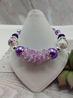 a purple beaded bracelet sitting on top of a white napkin next to a succulent plant