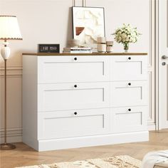 a white dresser sitting in a living room next to a lamp