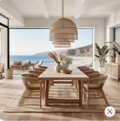 a dining room table with chairs and a vase on it in front of a large window overlooking the ocean