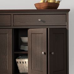 a wooden cabinet with two doors and some bowls on top of it, in front of a gray wall