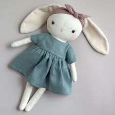 a stuffed rabbit in a blue dress laying on top of a white wall next to a pair of scissors