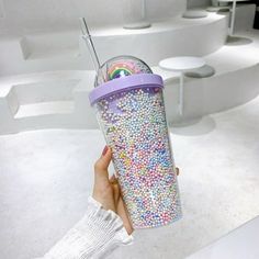 a hand holding a cup filled with lots of sprinkles on top of a white floor