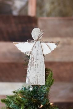 an angel ornament on top of a christmas tree in front of a wooden wall