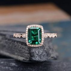 an emerald and diamond ring sitting on top of a black stone slab with diamonds around it