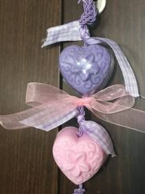 two heart shaped soaps hanging from a hook on a wooden table with ribbon and bow