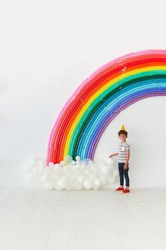 a young boy standing in front of a rainbow balloon arch