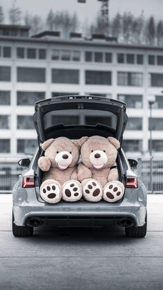 two teddy bears are sitting in the trunk of a car that is parked outside an apartment building