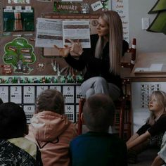 a woman standing in front of a group of children sitting down and reading to them