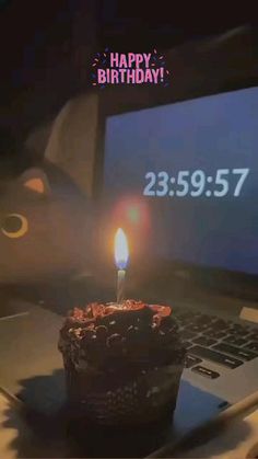 a birthday cupcake sitting on top of a laptop computer with a lit candle in front of it