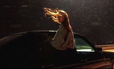 a woman sitting in the back of a car on a rainy night with her hair blowing in the wind