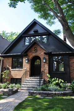 a brick house with black shingles and stone steps leading up to the front door