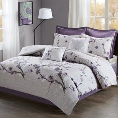 a bed with purple and white comforters in a room next to a lamp on a table